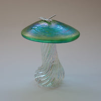 silver dragonfly resting on an iridescent green capped handmade glass toadstool
